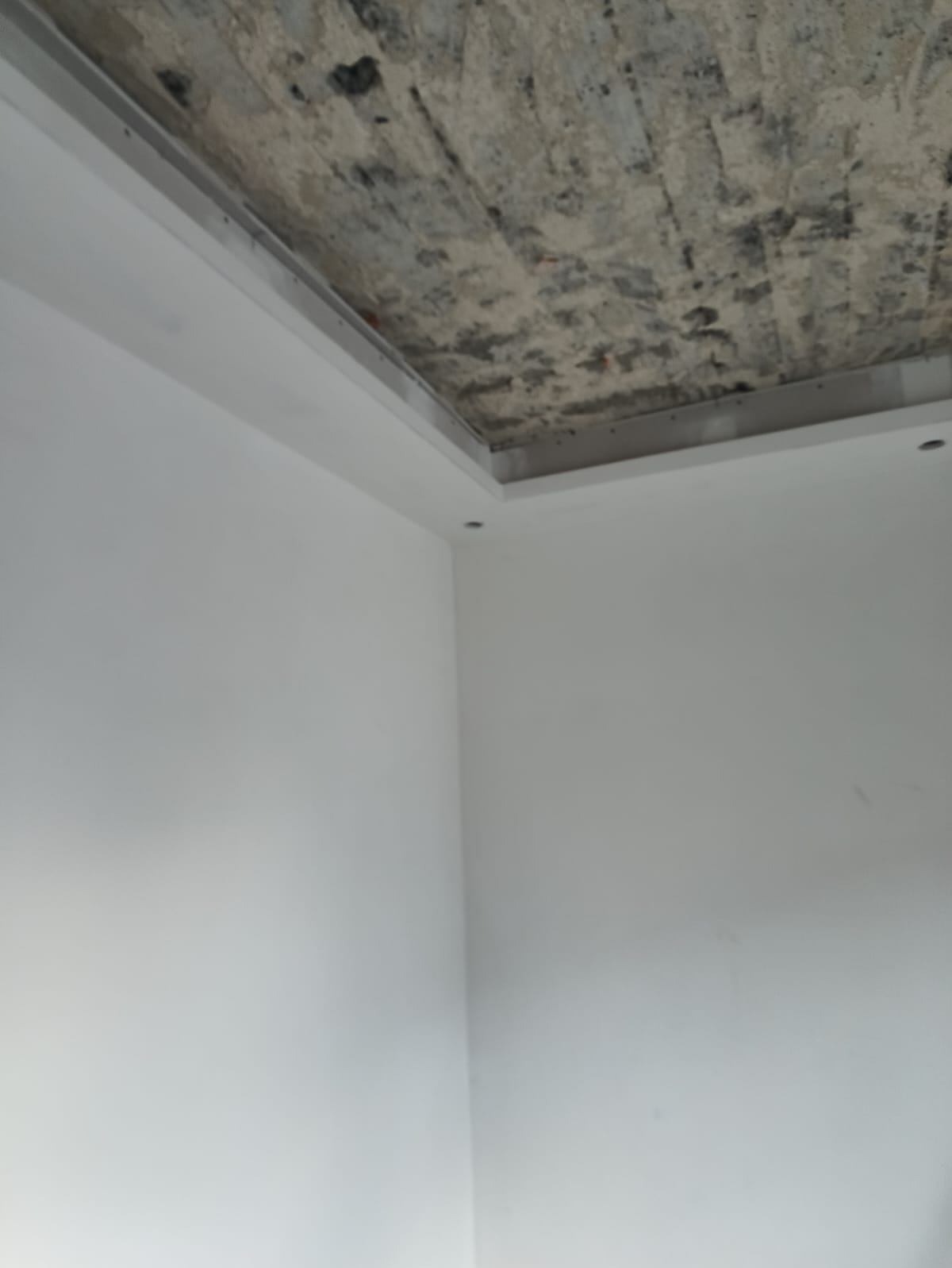 Ściana po gładziowaniu i malowaniu na biało, widoczny surowy betonowy sufit z obramowaniem. Detal wykończenia wnętrza.