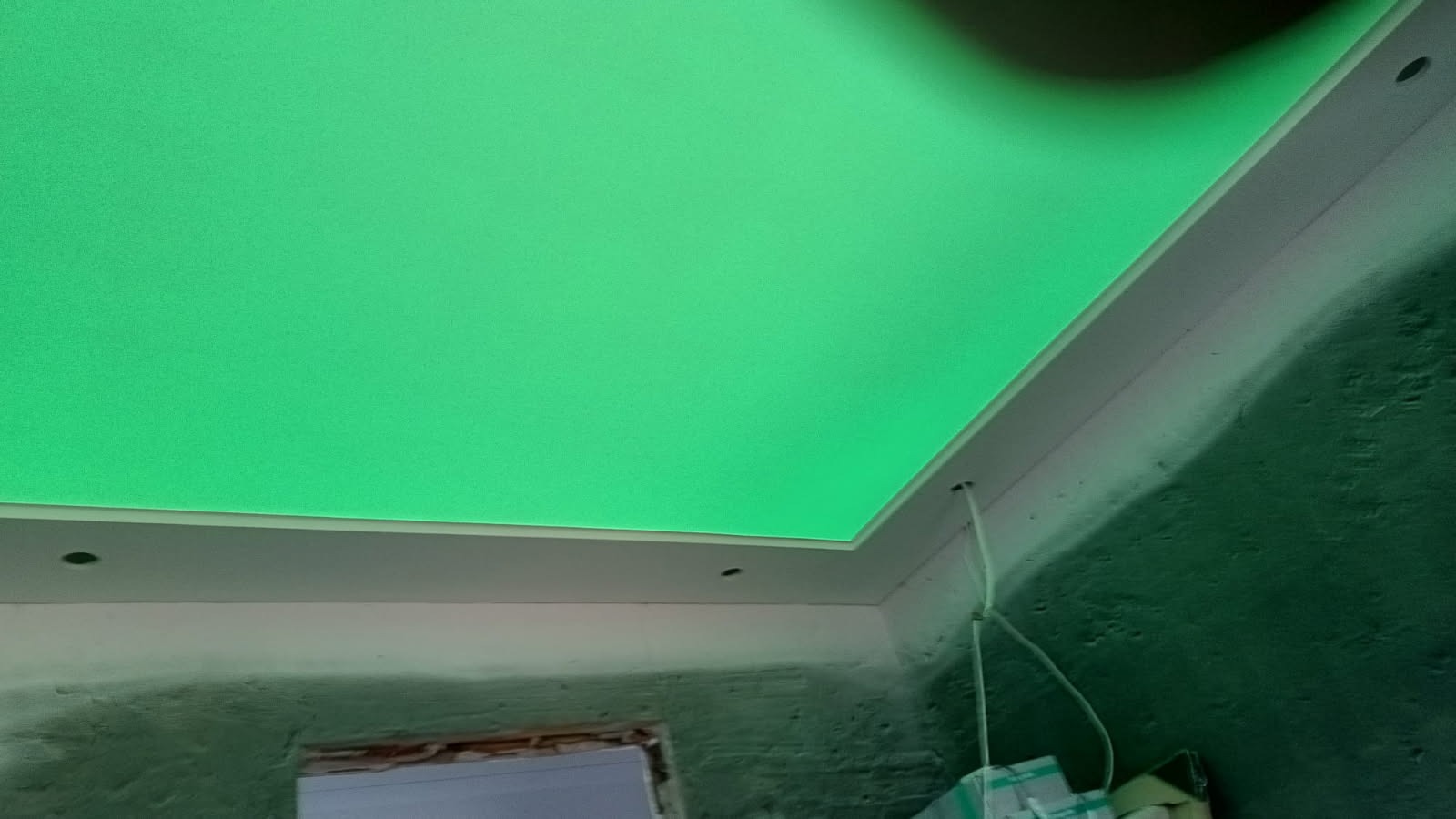 Podwieszany sufit z oświetleniem LED w odcieniu zieleni, widoczne niedokończone ściany i instalacja elektryczna. Kąt ujęcia z dołu, podkreślający efekt świetlny.