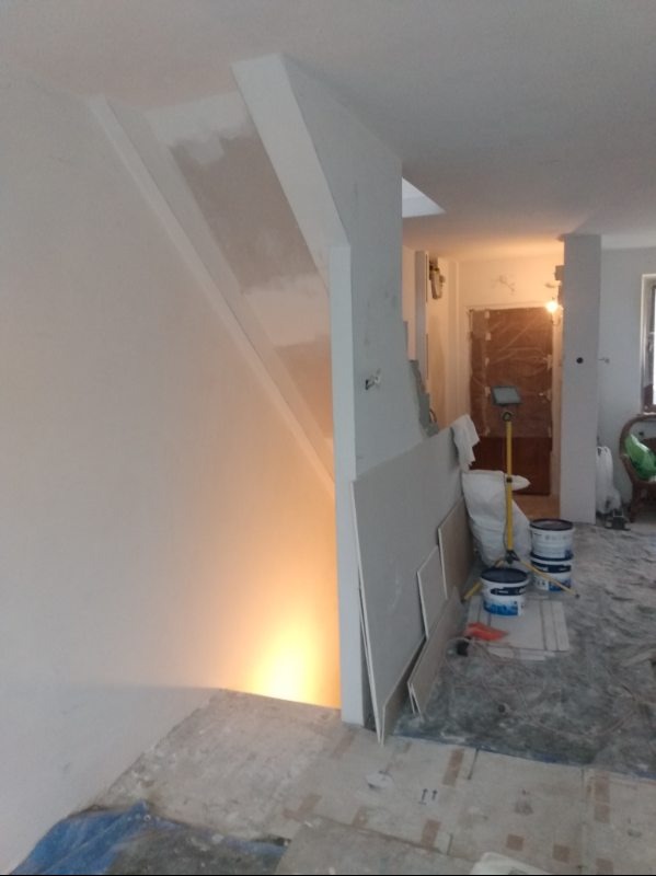 Wnętrze w trakcie prac wykończeniowych: ściany przygotowane pod malowanie, widoczne płyty karton-gips, podłoga zabezpieczona folią, puszki z farbą.