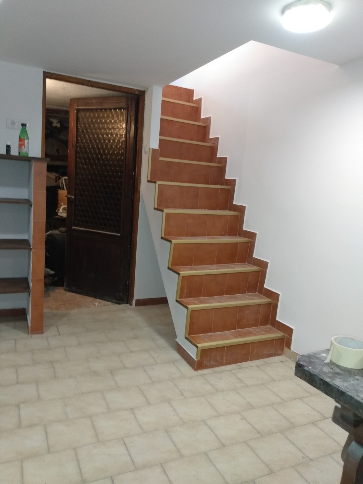 Wykończone schody z terakoty w piwnicy, widoczne płytki na podłodze i fragment otwartych drzwi do pomieszczenia gospodarczego. Świeżo pomalowane ściany.