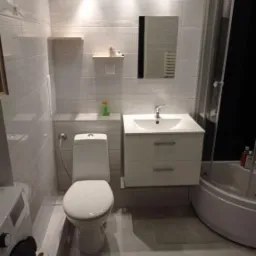 Jasna łazienka z płytkami imitującymi kamień, podwieszana szafka z umywalką, toaleta, kabina prysznicowa z ciemnym wnętrzem i półkami na ścianie.