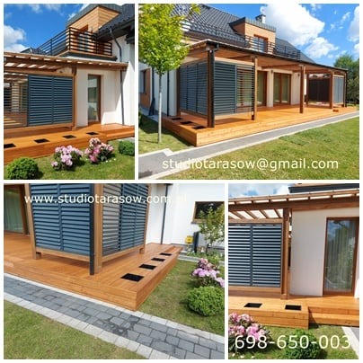 Rozległy, jasny taras z drewna z ażurowymi panelami zacieniającymi, przylegający do nowoczesnego domu z balkonem, otoczony zielonym trawnikiem i różowymi kwiatami.