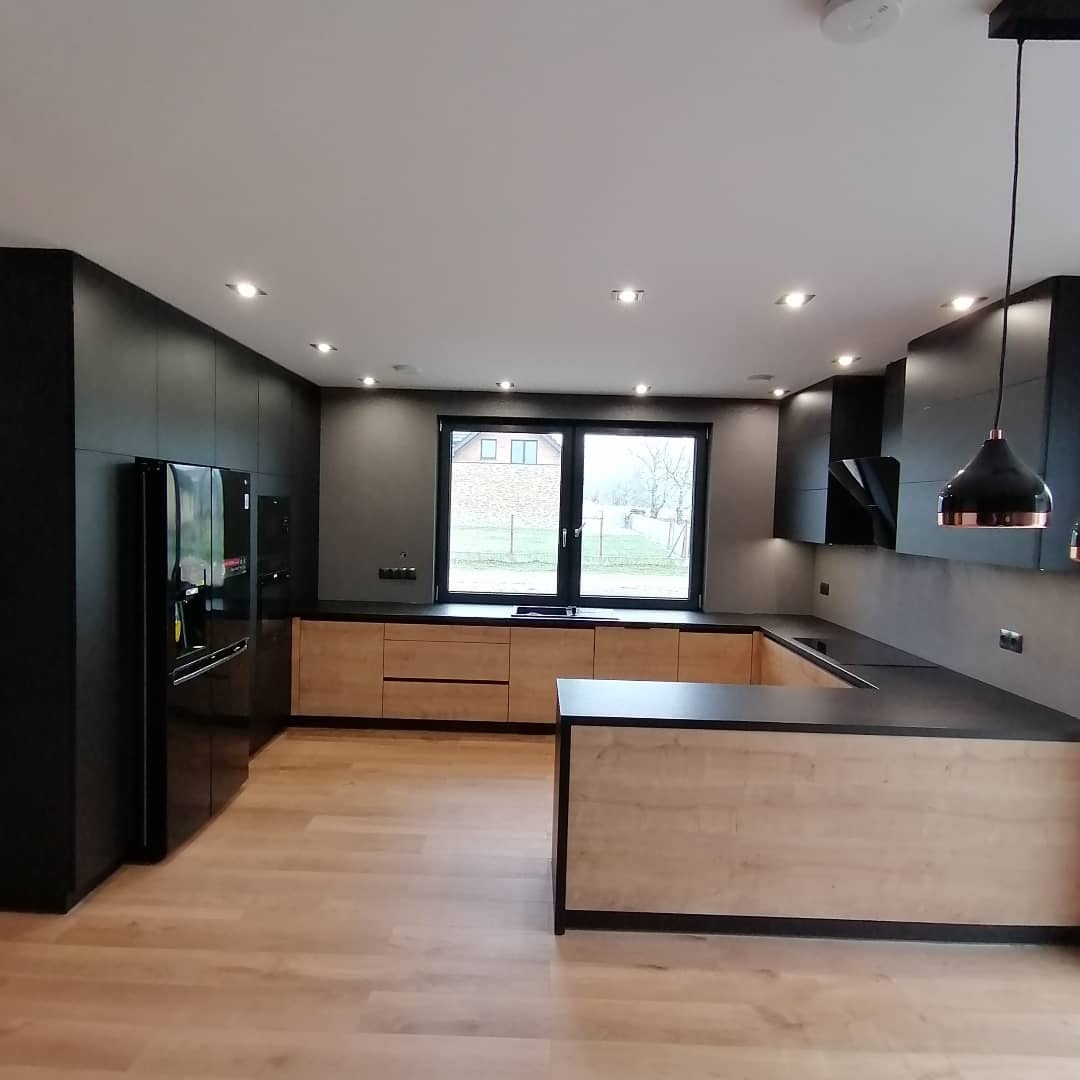 Nowoczesna kuchnia z drewnianymi frontami szafek dolnych i czarnymi szafkami górnymi oraz wyspą, czarny blat, drewniana podłoga, okno z widokiem na ogród.