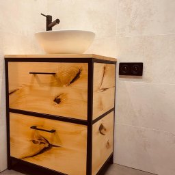 Kowadu Pracownia Sztuki Rzemiosła - Łazienkowa szafka pod umywalkę z dwiema szufladami, wykonana z jasnego drewna z wyraźnymi słojami i czarną, metalową ramą, na której stoi biała, okrągła umywalka z czarną armaturą. W tle beżowe...