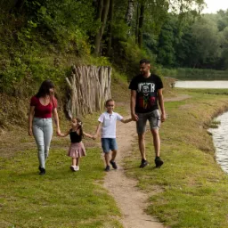 Rodzina z dwójką dzieci spaceruje ścieżką wzdłuż jeziora, tata w koszulce z Jokerem.
