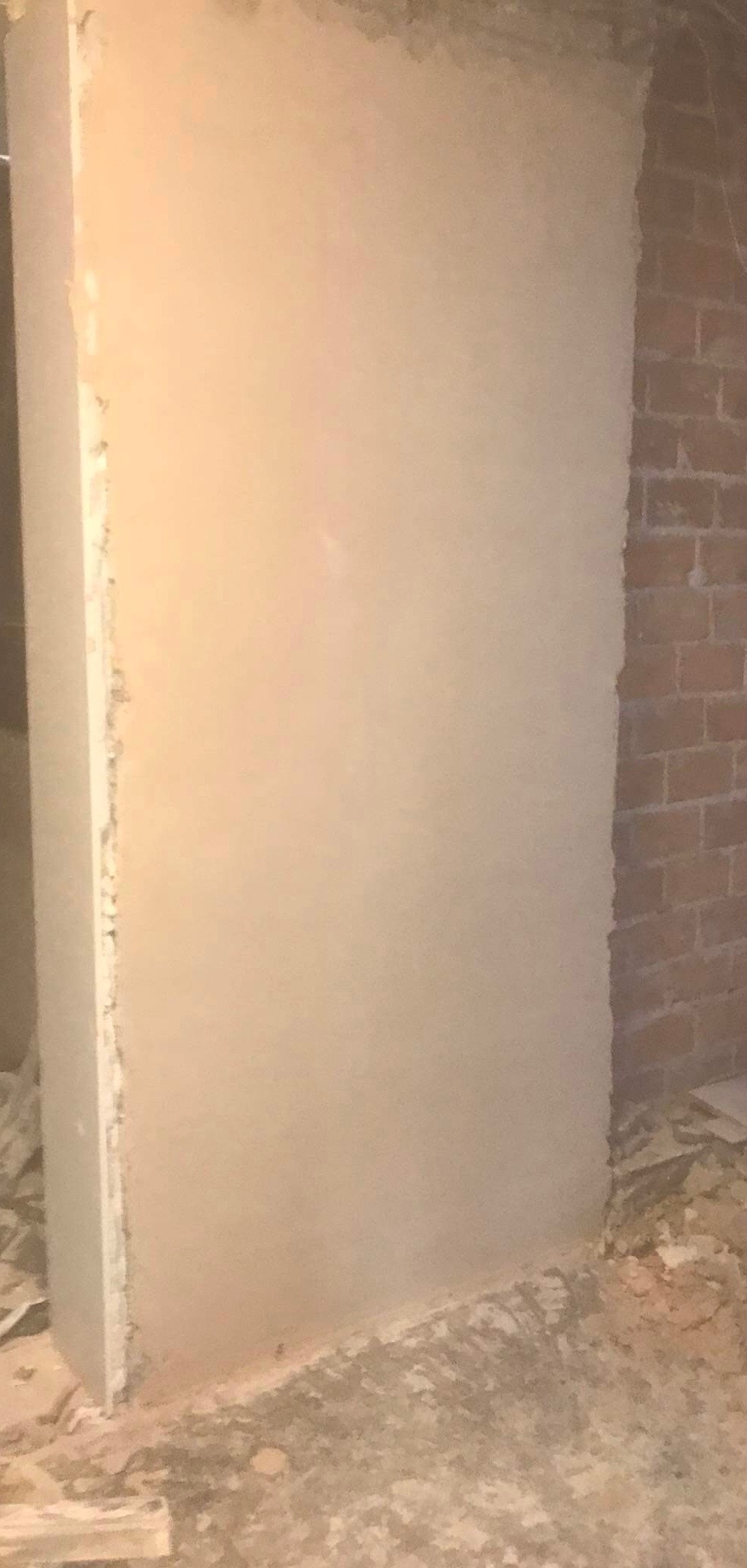 Ściana po szpachlowaniu, widoczna surowa cegła w rogu, przygotowana do dalszych prac wykończeniowych.