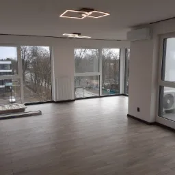 Nowe panele podłogowe imitujące drewno w jasnym, przestronnym pokoju w Legnicy, z widocznymi listwami przypodłogowymi i nowoczesnym oświetleniem sufitowym.