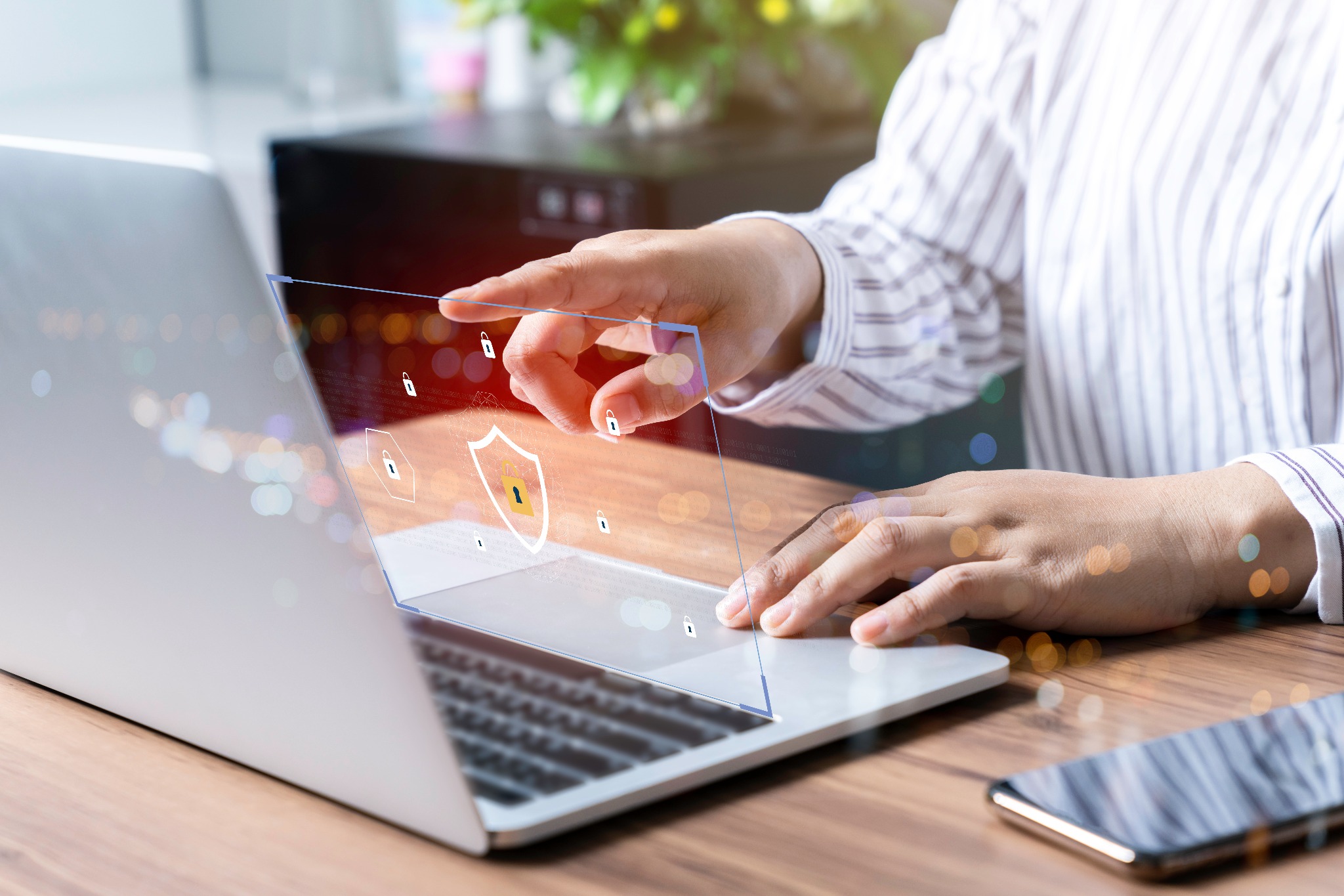 Osoba dotyka ekranu laptopa z wyświetlaną grafiką tarczy i kłódek, symbolizującą bezpieczeństwo danych w sieci.