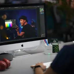 Osoba edytuje zdjęcie piosenkarza na iMacu z otwartym panelem kolorów, obok słuchawki i telefon w stacji dokującej Google Partners.