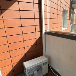 Eko-Klima Krzysztof Żochowski - Biała jednostka zewnętrzna klimatyzacji Hisense Inverter Expert zamontowana na balkonie, z widocznym odpływem i przewodami, na tle pomarańczowej elewacji budynku.