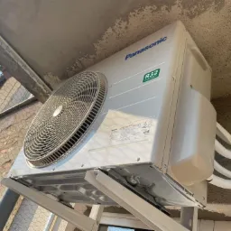 Zamontowana jednostka zewnętrzna klimatyzacji Panasonic R32 na balkonie we Wrocławiu, widok od dołu na wsporniki i rury chłodnicze, siatka zabezpieczająca balkon w tle.