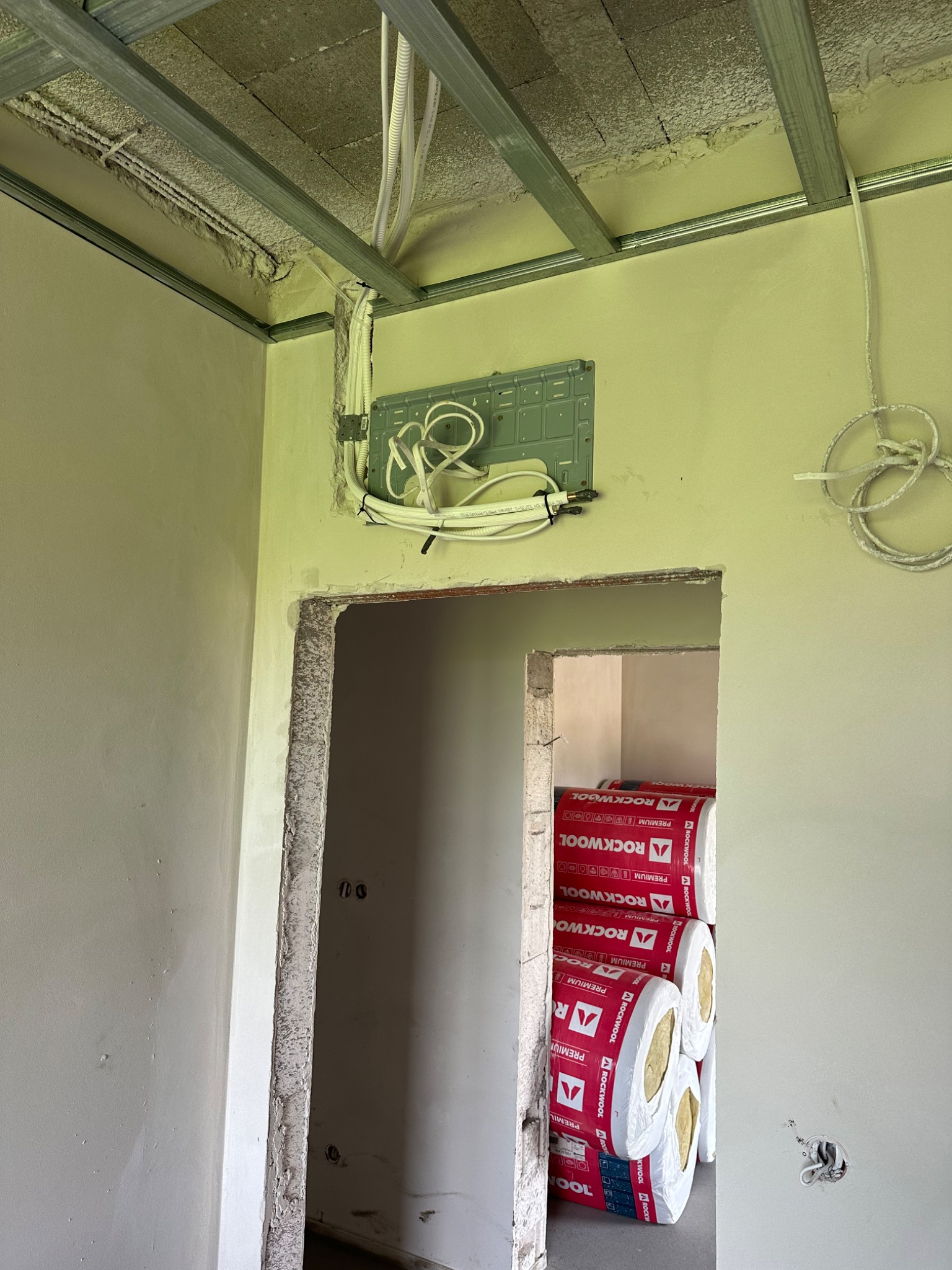 Instalacja elektryczna w trakcie montażu w nowym budynku, widoczne kable, puszka instalacyjna, stelaż sufitu podwieszanego i izolacja Rockwool w sąsiednim pomieszczeniu.