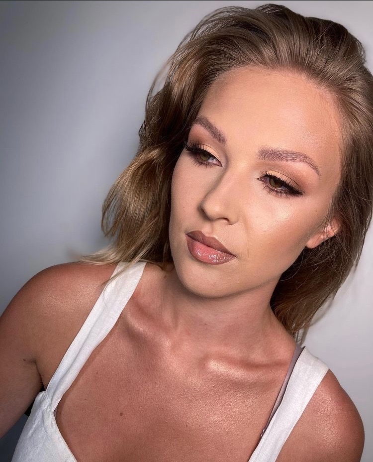 Portret kobiety z delikatnym makijażem nude, podkreślone brwi i usta z błyszczykiem, subtelne cieniowanie powiek, włosy w odcieniach blondu.