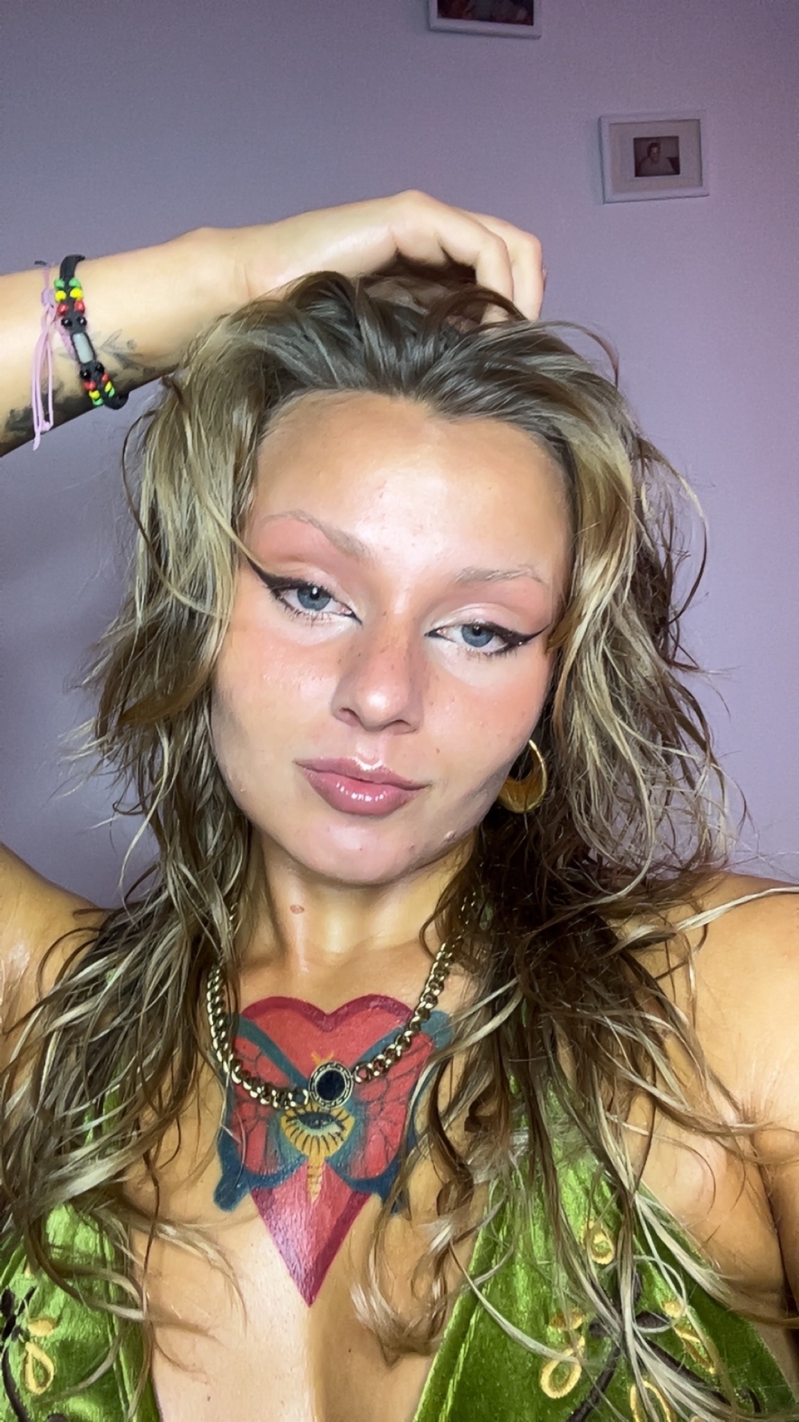 Portret kobiety z wyrazistym makijażem oczu i ust, podkreślonymi kośćmi policzkowymi i tatuażem na dekolcie, w blasku światła.