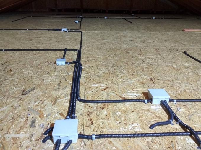 Instalacja elektryczna w peszlach prowadzona po drewnianej płycie OSB na poddaszu, widoczne puszki instalacyjne.