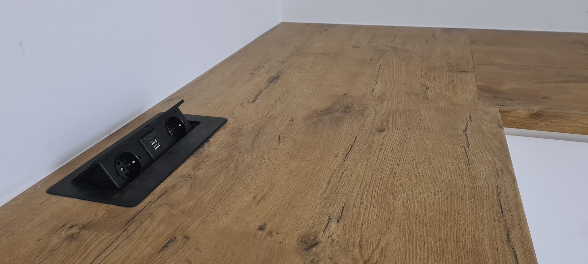 Blat drewniany z wbudowanym, czarnym gniazdkiem elektrycznym z dwoma gniazdami i portami USB, widoczne słoje drewna.