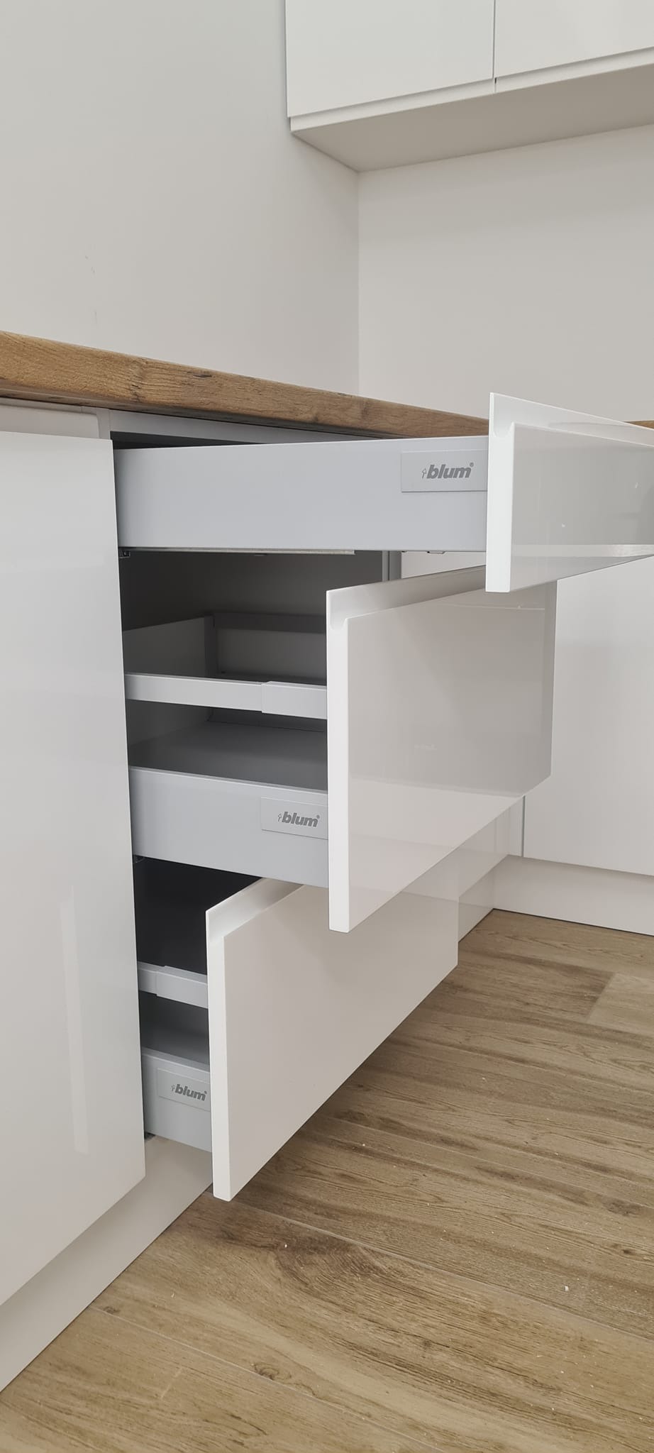 Biała, lakierowana zabudowa kuchenna z otwartymi szufladami marki Blum, widoczne półki wewnątrz szuflad, blat drewniany.