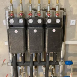 Rozdzielacze ogrzewania podłogowego z manometrami i zaworami, zamontowane na ścianie w Majdanie Królewskim, widoczne rury w izolacji i instalacja hydrauliczna.