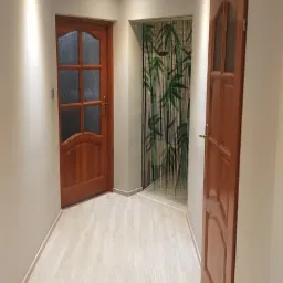 Jasne panele podłogowe w przedpokoju z dwiema drewnianymi, przeszklonymi drzwiami i ozdobną zasłoną z motywem bambusa.