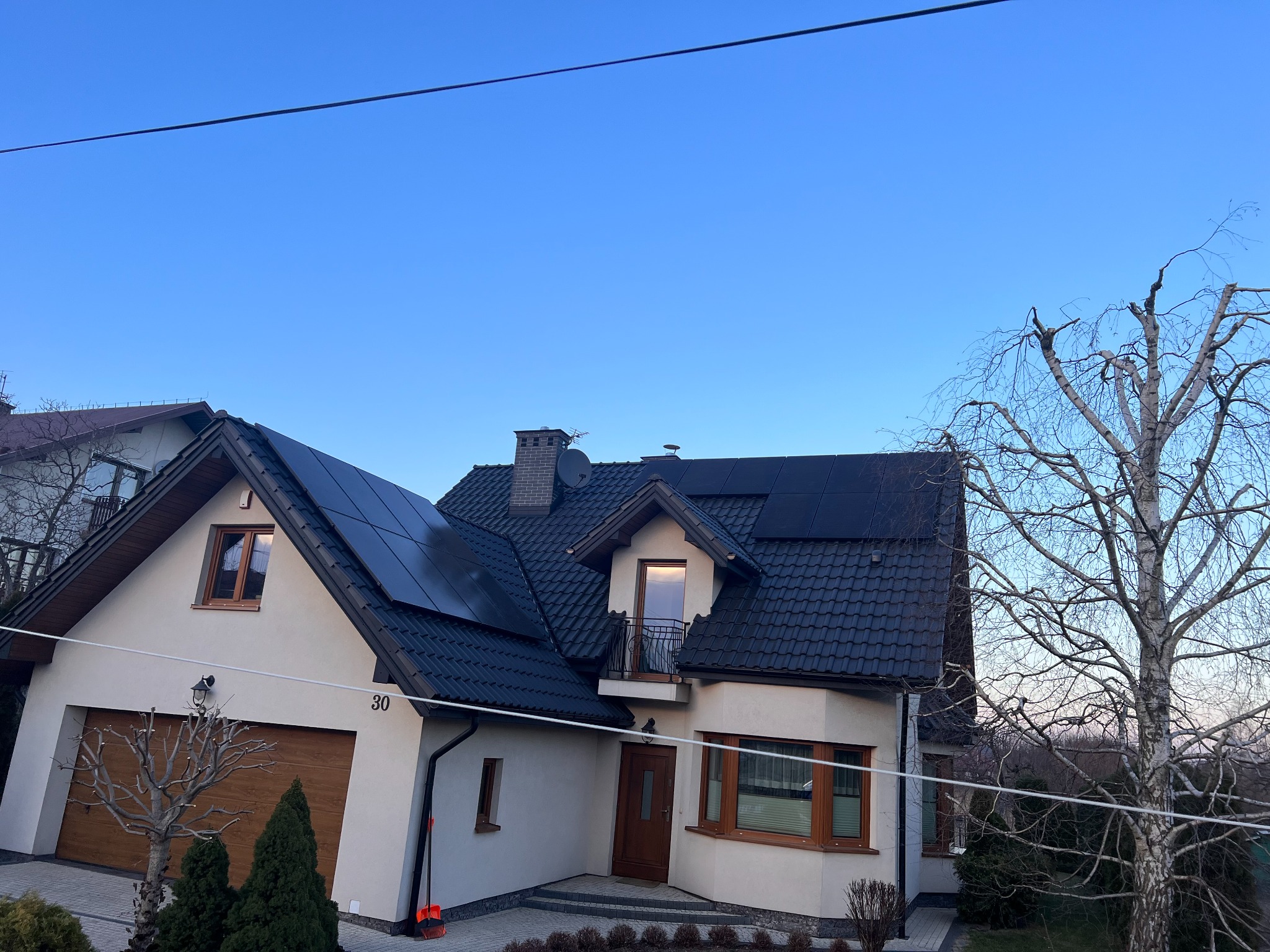 Dom jednorodzinny z panelami słonecznymi na dachu, widok z zewnątrz w pogodny dzień, widoczny numer domu '30'.