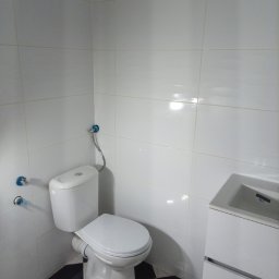 Łukrem - Biała toaleta z umywalką w szafce na tle białych płytek i czarno-białej szachownicy na podłodze.