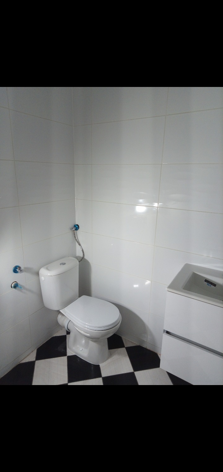 Biała toaleta z umywalką w szafce na tle białych płytek i czarno-białej szachownicy na podłodze.