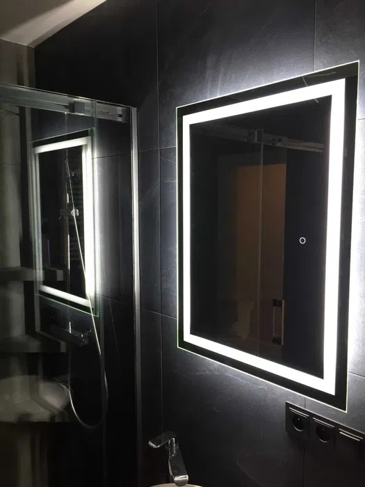 Nowoczesna łazienka z czarnymi płytkami, oświetlonym lustrem i szklaną kabiną prysznicową z chromowaną armaturą.