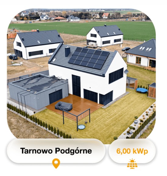 Widok z góry na nowoczesny dom z panelami słonecznymi na dachu, drewnianym tarasem i minimalistycznym ogrodem, otoczony innymi domami w Tarnowie Podgórnym.