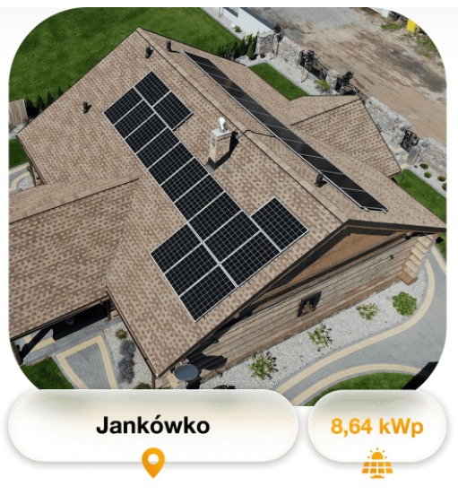 Widok z góry na brązowy dach domu z panelami słonecznymi w układzie blokowym, komin na dachu i zagospodarowany teren wokół domu.