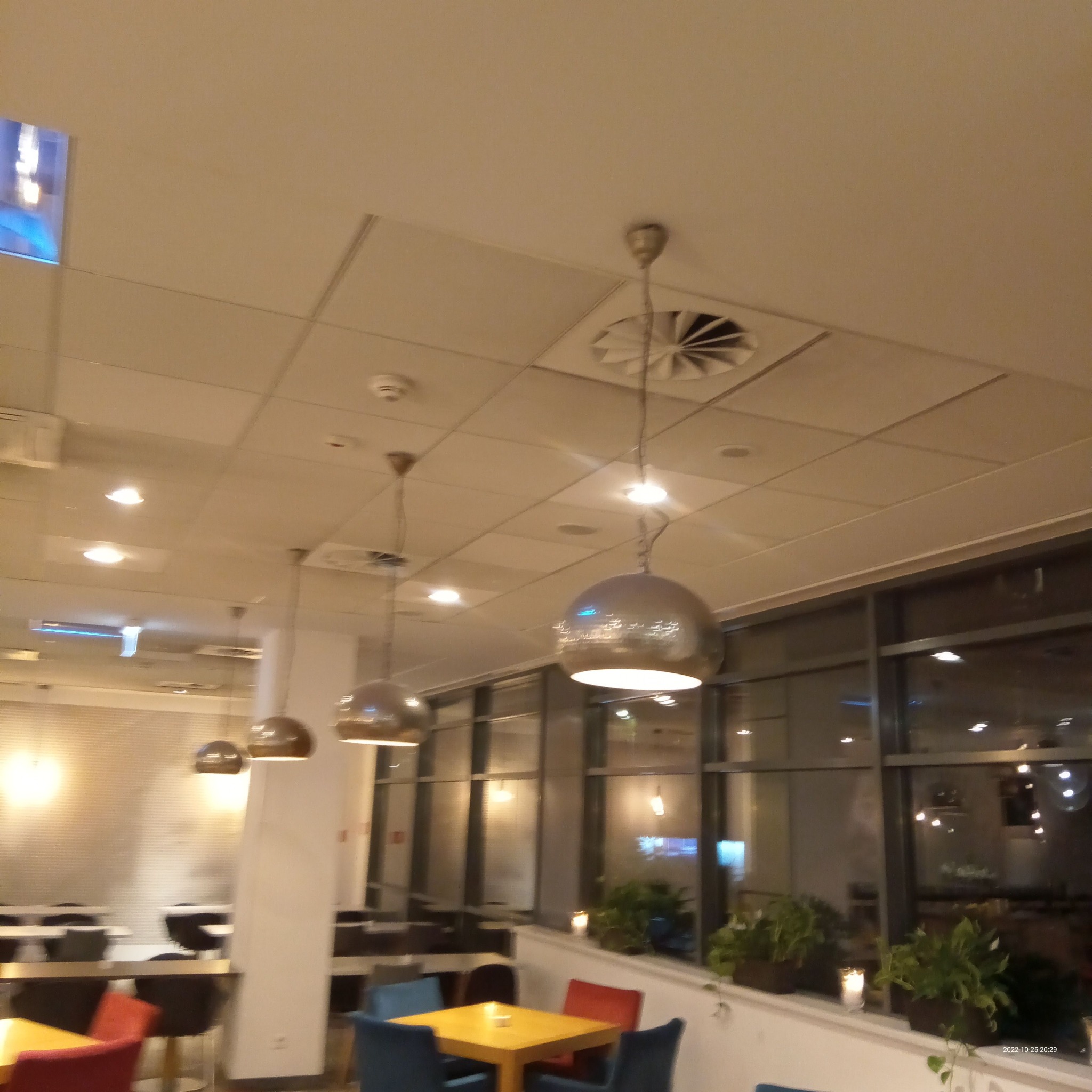 Wnętrze biura z widocznymi lampami kulistymi, stolikami z krzesłami oraz roślinami doniczkowymi na parapecie okiennym.