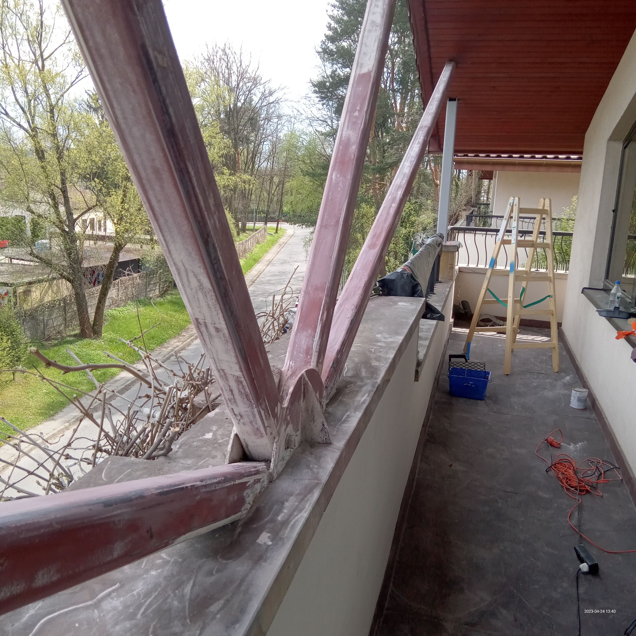 Metalowa konstrukcja wspornikowa balkonu w trakcie przygotowania do malowania, widoczne ślady szpachlowania, w tle drabina malarska i narzędzia.