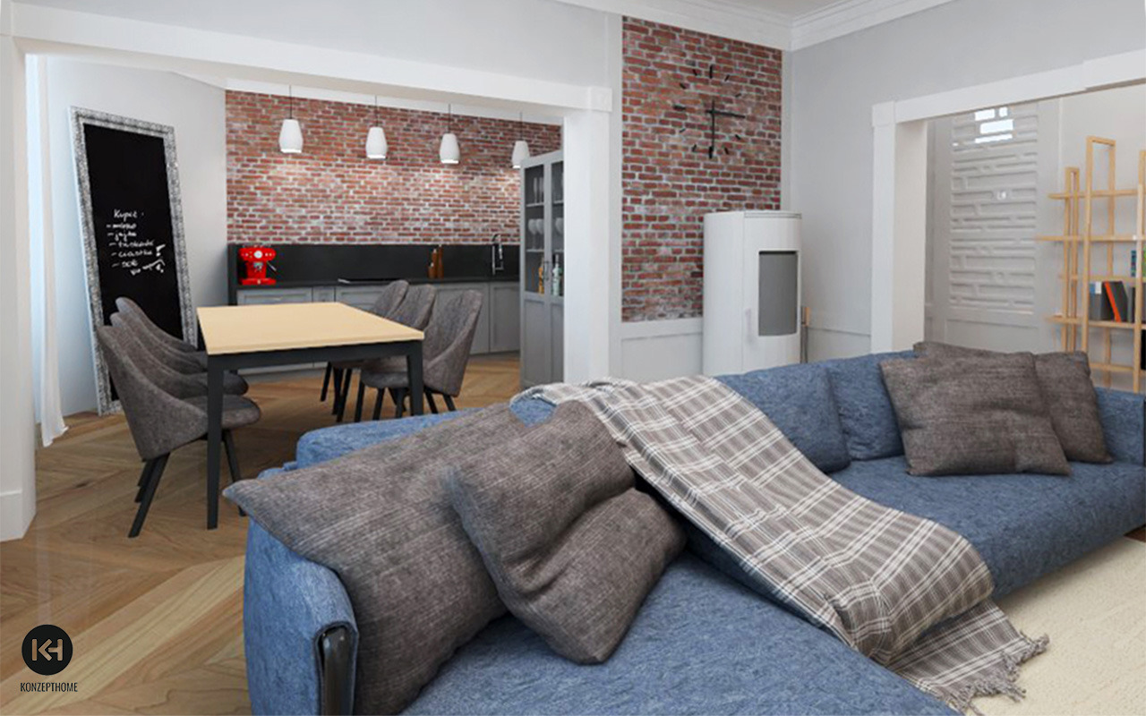 Salon z ceglaną ścianą, niebieską sofą z poduszkami i pledem w kratę, otwarta kuchnia w tle, drewniana podłoga w jodełkę.