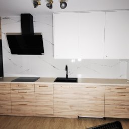 Ewkon - Nowoczesna kuchnia z frontami w odcieniach drewna i białymi szafkami wiszącymi, czarny okap i armatura, marmurowe płytki na ścianie, oświetlenie punktowe.