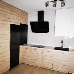 Ewkon - Nowoczesna kuchnia w Paterek z drewnianymi frontami, czarnym sprzętem AGD i marmurowym backsplashiem. Minimalistyczny design, złote uchwyty.
