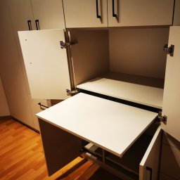 Ewkon - Biała szafa na wymiar z rozkładanym blatem, otwarte drzwiczki ukazują mechanizm. Widoczne minimalistyczne uchwyty i drewniana podłoga.