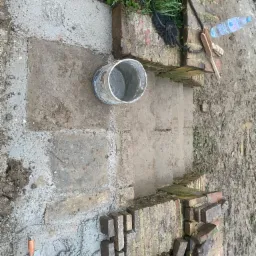 Budowa ceglanych schod&oacute;w zewnętrznych z użyciem zaprawy, widoczne narzędzia murarskie, wiadro z zaprawą i butelka wody obok