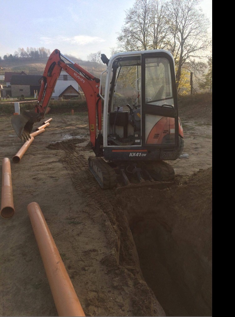 Mini koparka Kubota KX41-3V w Stężycy przygotowuje wykop pod rury kanalizacyjne; pomarańczowe rury leżą obok wykopu.