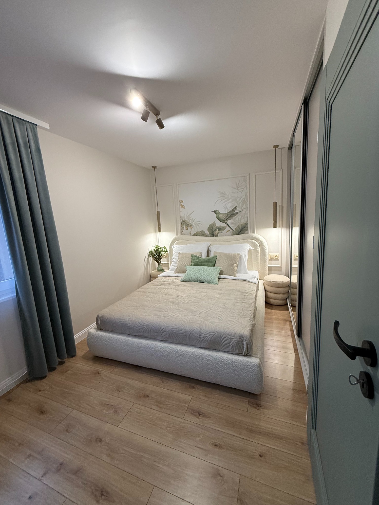 Jasna sypialnia w Białym Dunajcu po remoncie: drewniana podłoga, łóżko z tapicerowanym zagłówkiem, przesuwne drzwi szafy i dekoracje w stylu botanicznym.