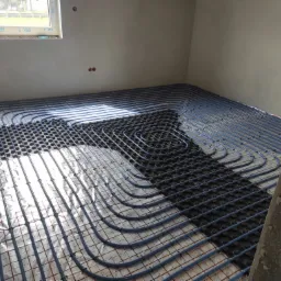 Niedokończona instalacja ogrzewania podłogowego w Lwówku Śląskim, widoczne rury grzewcze ułożone na folii z rastrem i elementami mocującymi, surowy stan ścian.