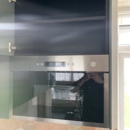 Dawid Szpejenkowski - Wbudowany piekarnik ze stali nierdzewnej zamontowany w szafce kuchennej; ściana w trakcie przygotowywania, widoczne ślady po szpachlowaniu.