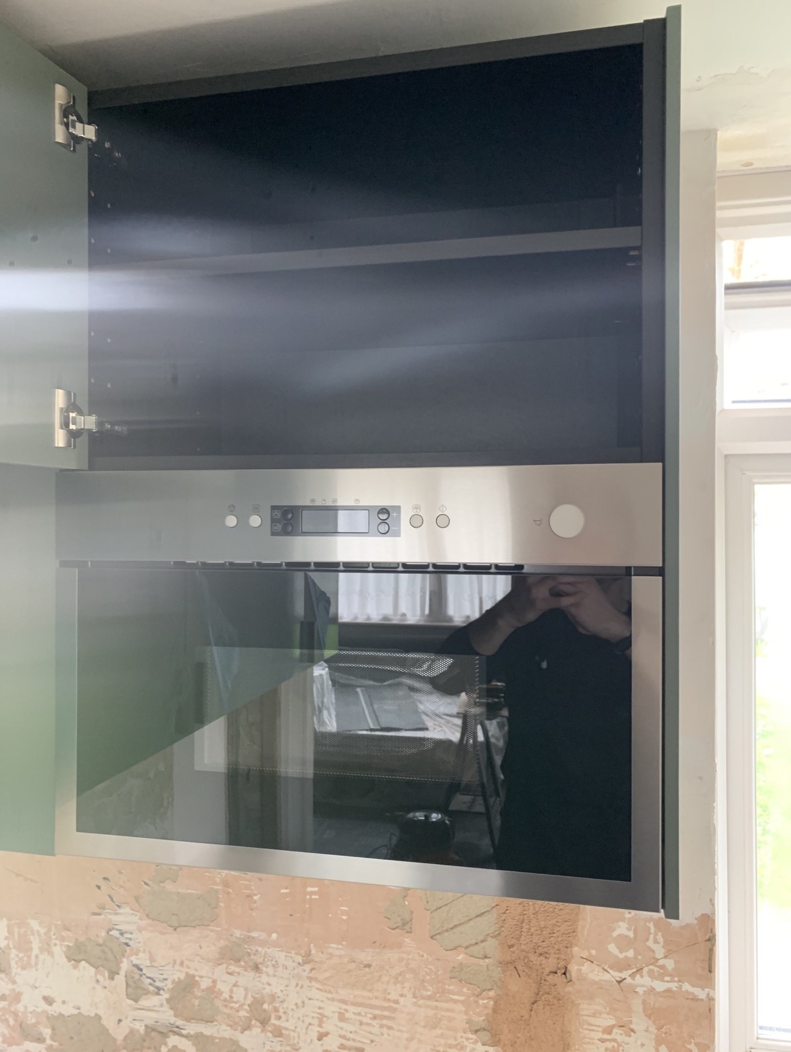 Wbudowany piekarnik ze stali nierdzewnej zamontowany w szafce kuchennej; ściana w trakcie przygotowywania, widoczne ślady po szpachlowaniu.