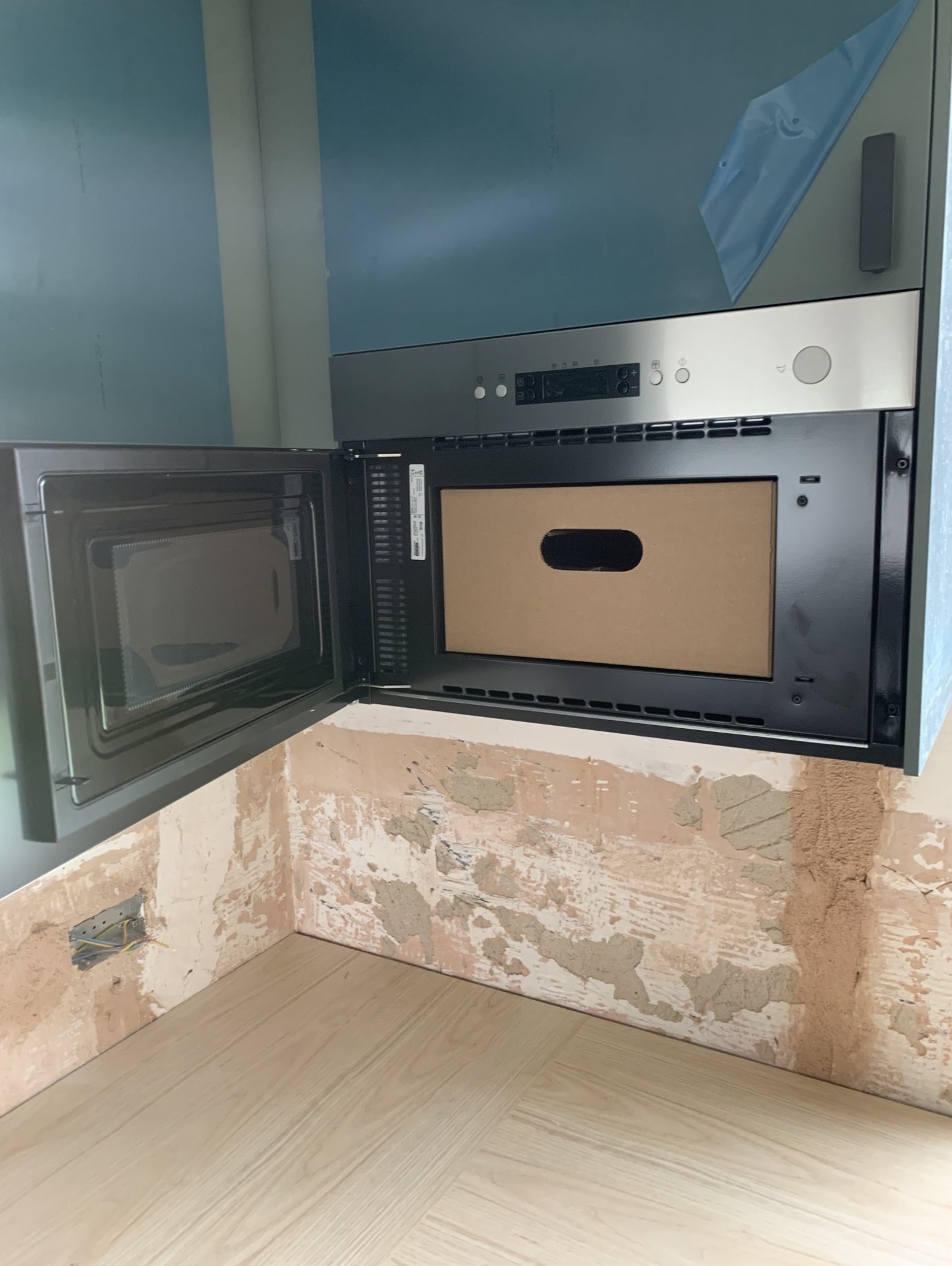 Wbudowana mikrofalówka w trakcie montażu, widoczne niedokończone ściany i nowa podłoga.