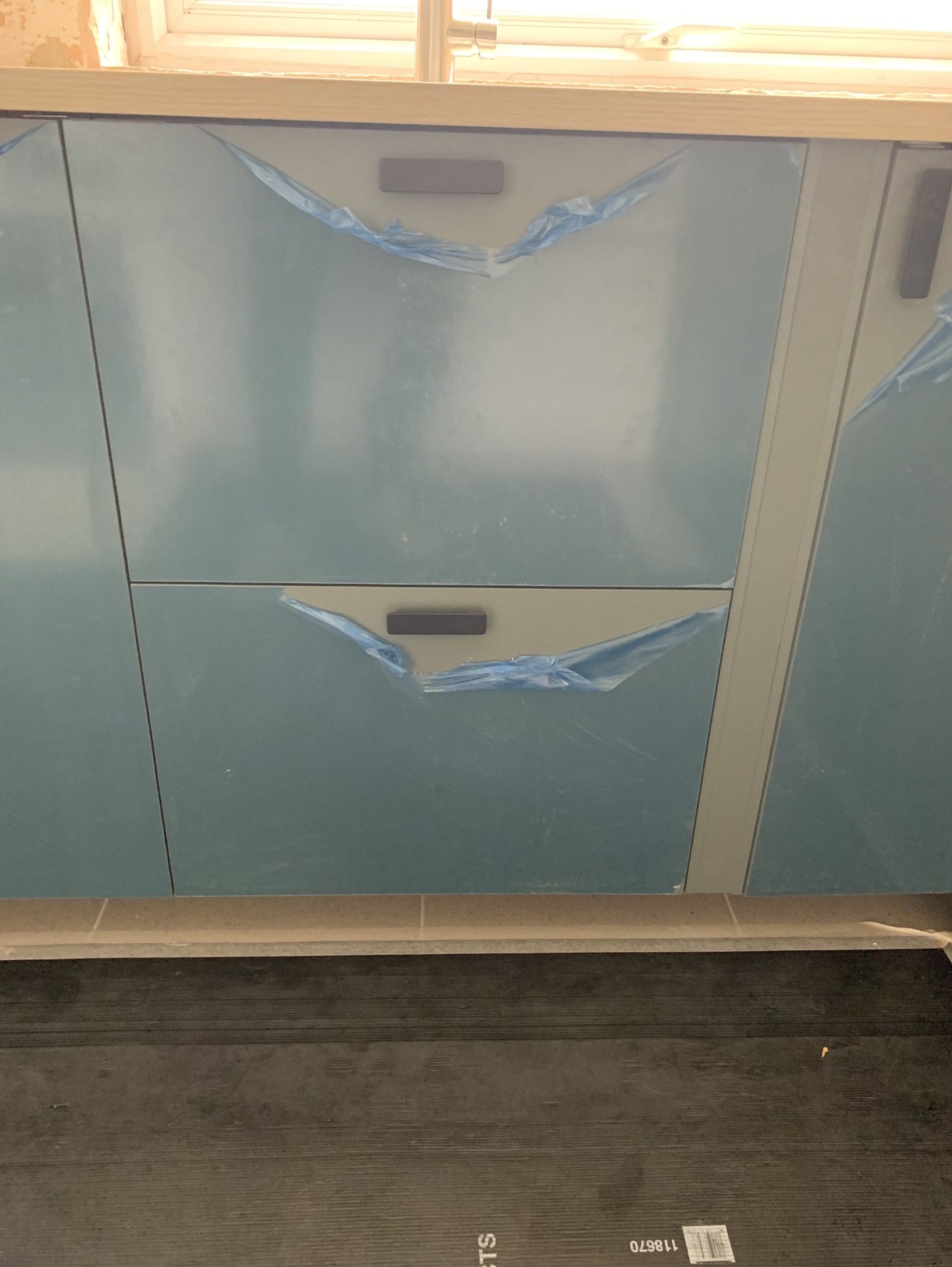 Niebieskie szafki kuchenne z szarymi uchwytami, zabezpieczone folią ochronną, widoczne podczas montażu.