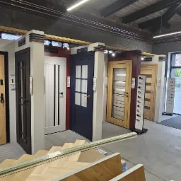 Ekspozycja różnorodnych drzwi wewnętrznych marki Erkado w salonie, prezentująca modele w różnych kolorach i stylach, z widocznymi elementami podłóg drewnianych.