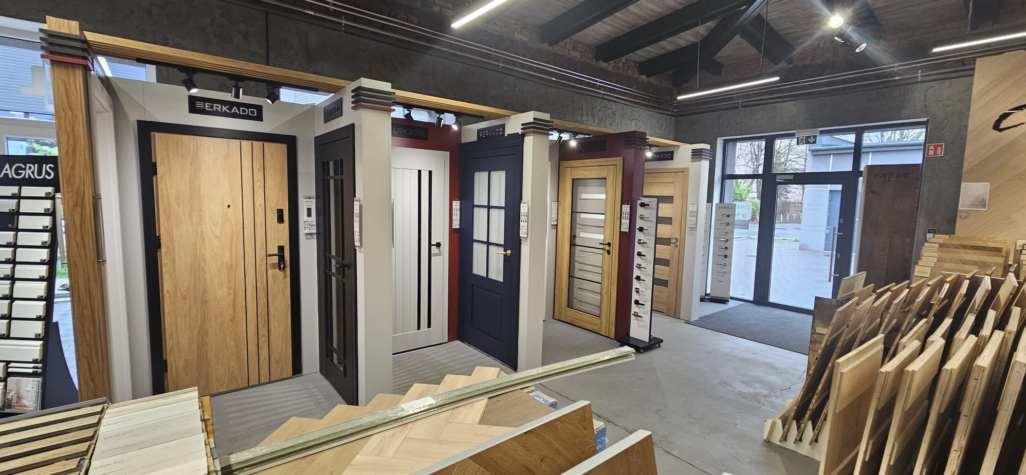 Ekspozycja różnorodnych drzwi wewnętrznych marki Erkado w salonie, prezentująca modele w różnych kolorach i stylach, z widocznymi elementami podłóg drewnianych.