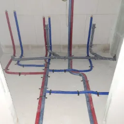 Rozprowadzenie instalacji wodnej z rur PEX w kolorze niebieskim i czerwonym, przymocowanych do podłoża. Szare rury kanalizacyjne złączone złączkami.