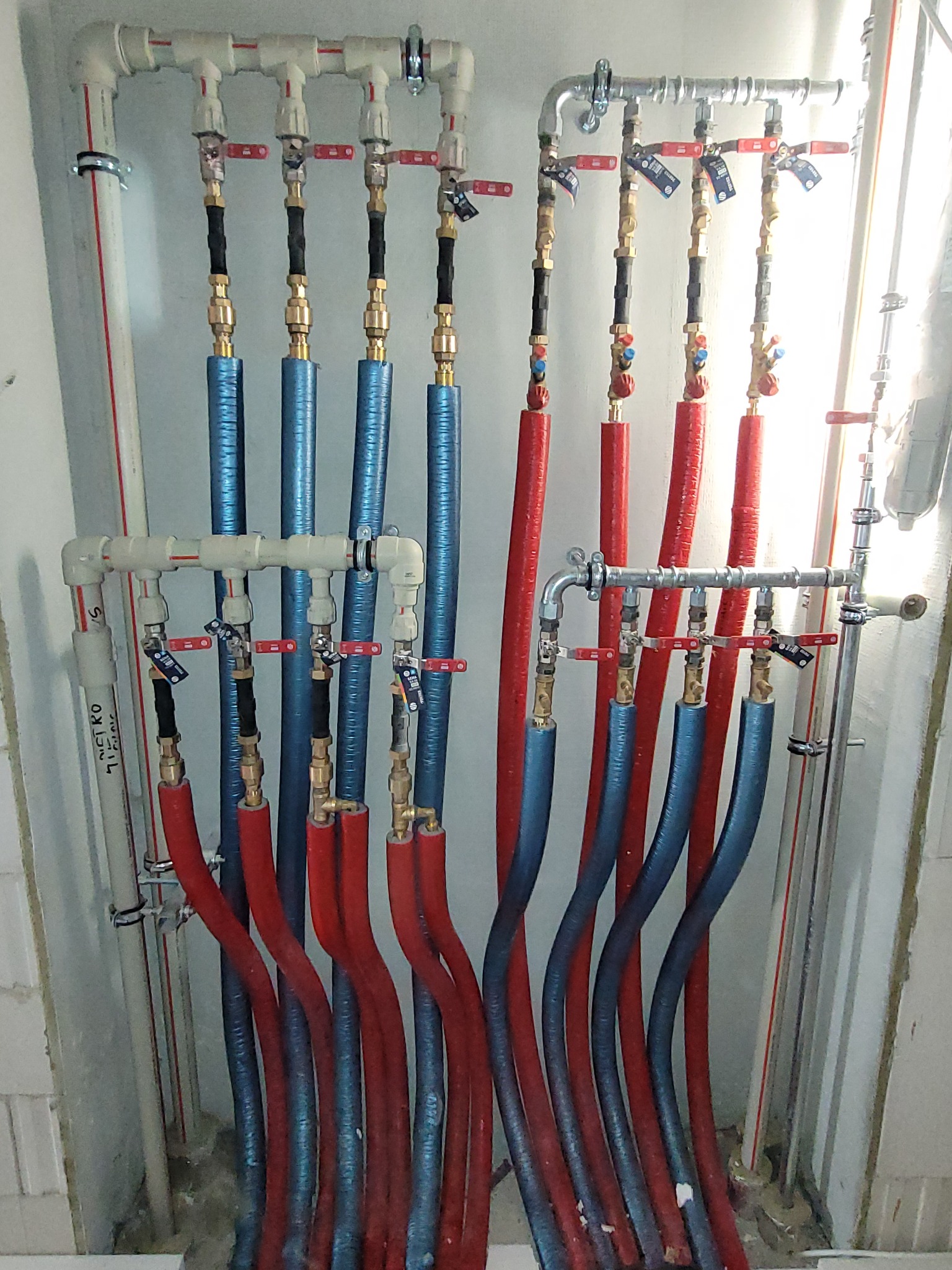 Rozdzielacz instalacji CO i CWU z rurami w izolacji, zamontowany w nowym budownictwie w Krakowie. Widoczne zawory i precyzyjne połączenia.