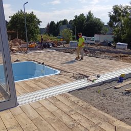 Arko-Bud - Układanie kostki brukowej imitującej drewno wokół basenu. Pracownik w kamizelce odblaskowej. Widoczne narzędzia i materiały budowlane.