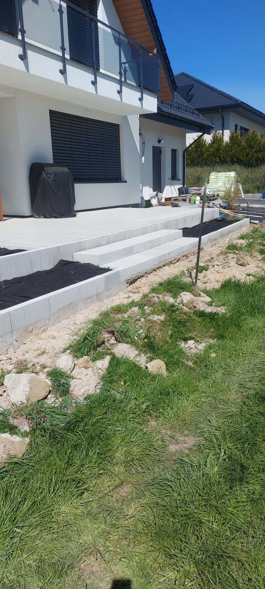 Jasnoszare, granitowe schody wejściowe do domu jednorodzinnego, z widocznym fragmentem tarasu i przygotowanym miejscem na rabatę kwiatową.