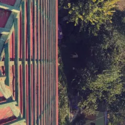 Częściowo zdemontowany czerwony dach z widoczną konstrukcją drewnianą na tle zieleni ogrodu.